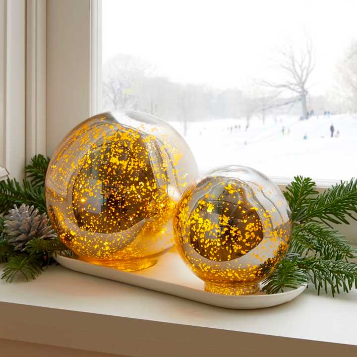 gold globe decorations with greenery in window