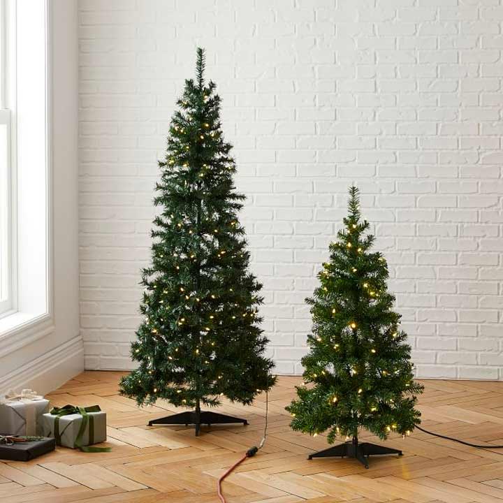 two small christmas trees with lights against white wall