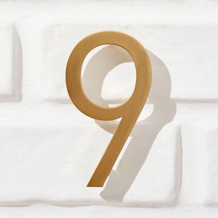 Brushed gold number 9 on white brick.