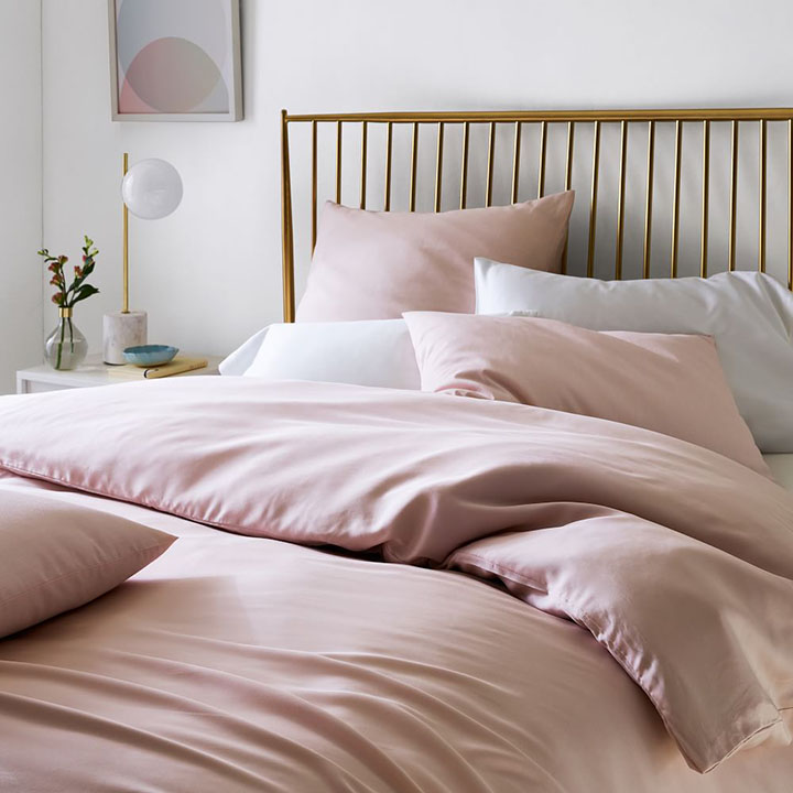 Brass spindle bed frame with pink comforter and pillows.