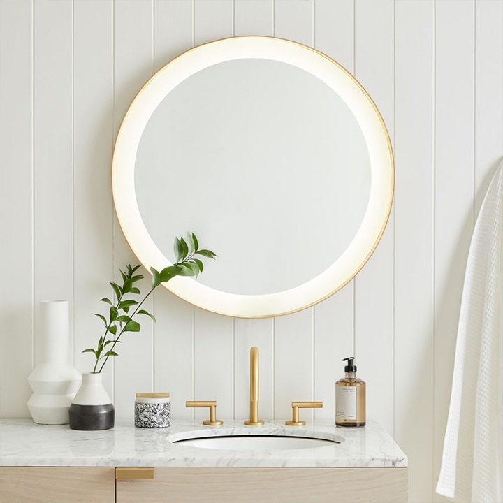 Round vanity mirror with built-in LED border over sink.