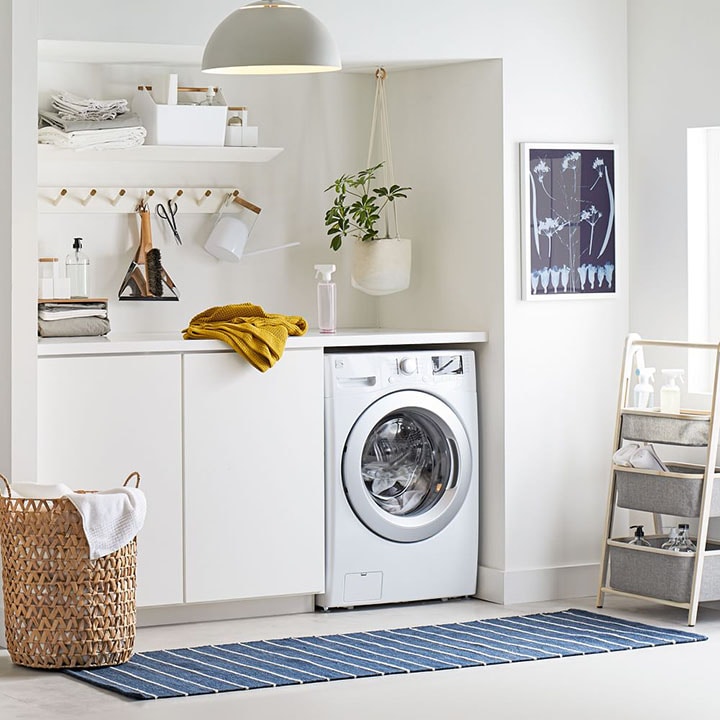 White washing machine in laundry room with blue striped rug and wicker laundry basket. White washing machine in laundry room with blue striped rug and wicker laundry basket.