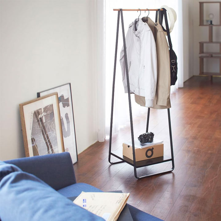 Modern clothing rack displaying clothing pieces next to blue sofa in a guest room. Modern clothing rack displaying clothing pieces next to blue sofa in a guest room.