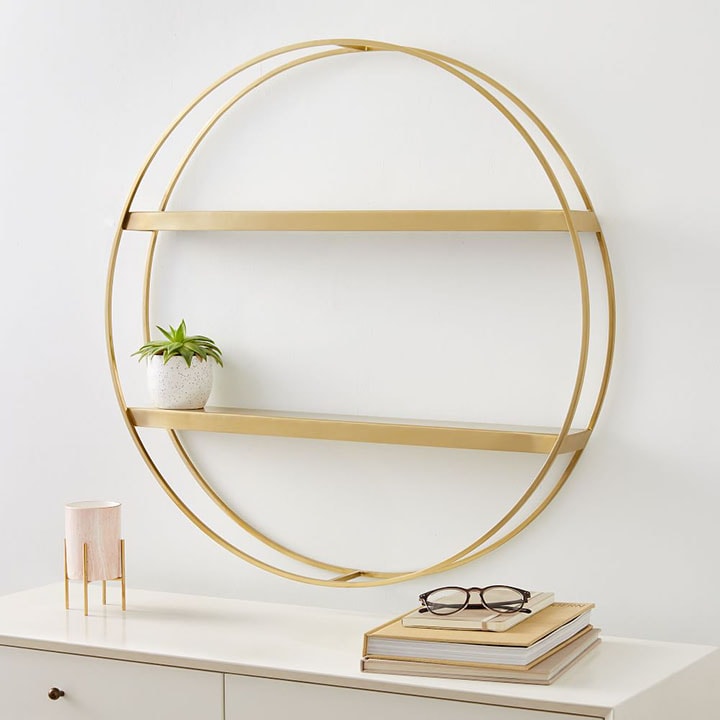 Gold round metal wall shelf hanging above a dresser.
