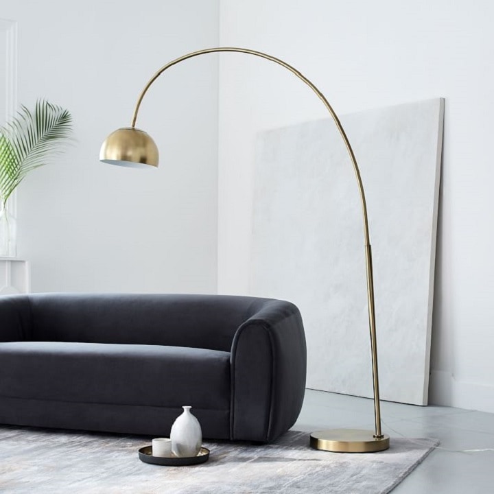 Overarching metal shade floor lamp next to velvet sofa