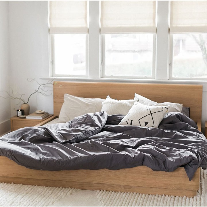 Bed in front of window with sheer curtains.