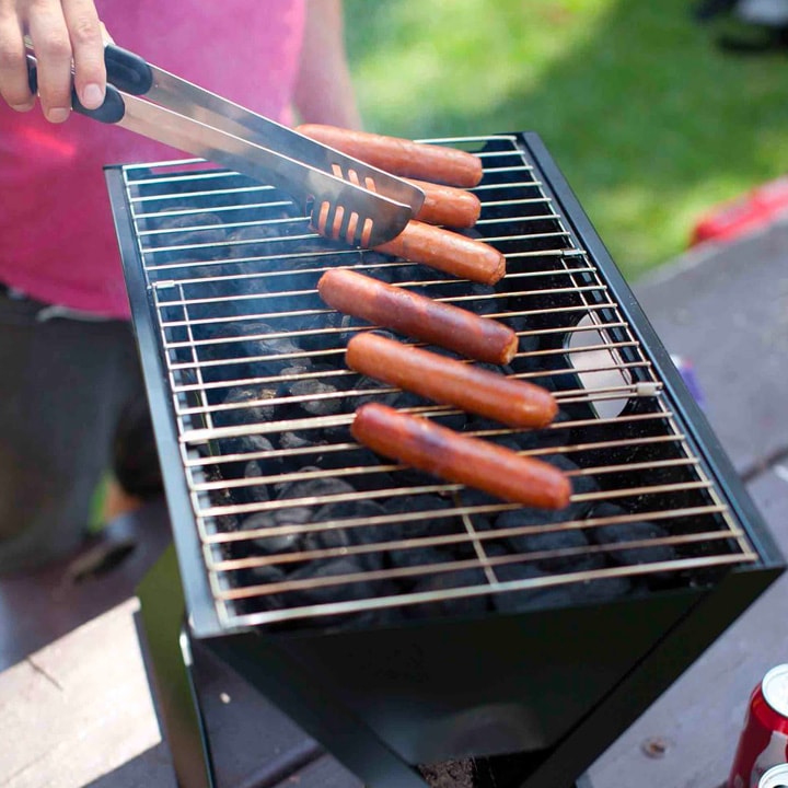 Man cooking hot dogs on portable grill.