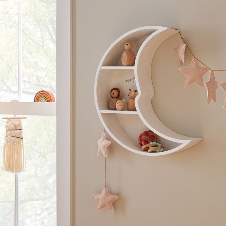 Moon-shaped shelf in nursery with pink felt stars.