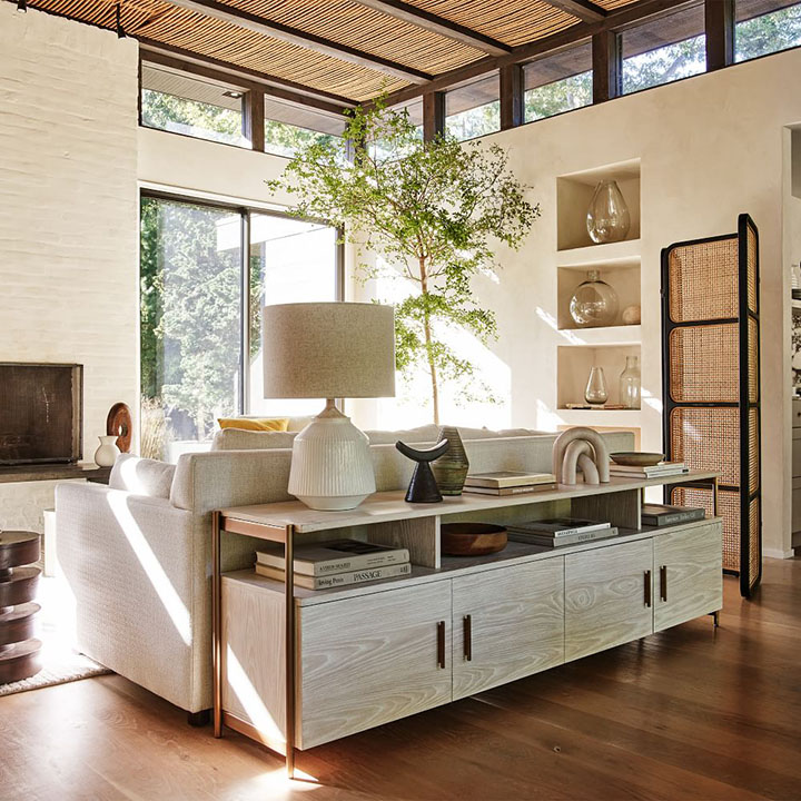 Media console with decorative objects behind white sofa near sunroom window.