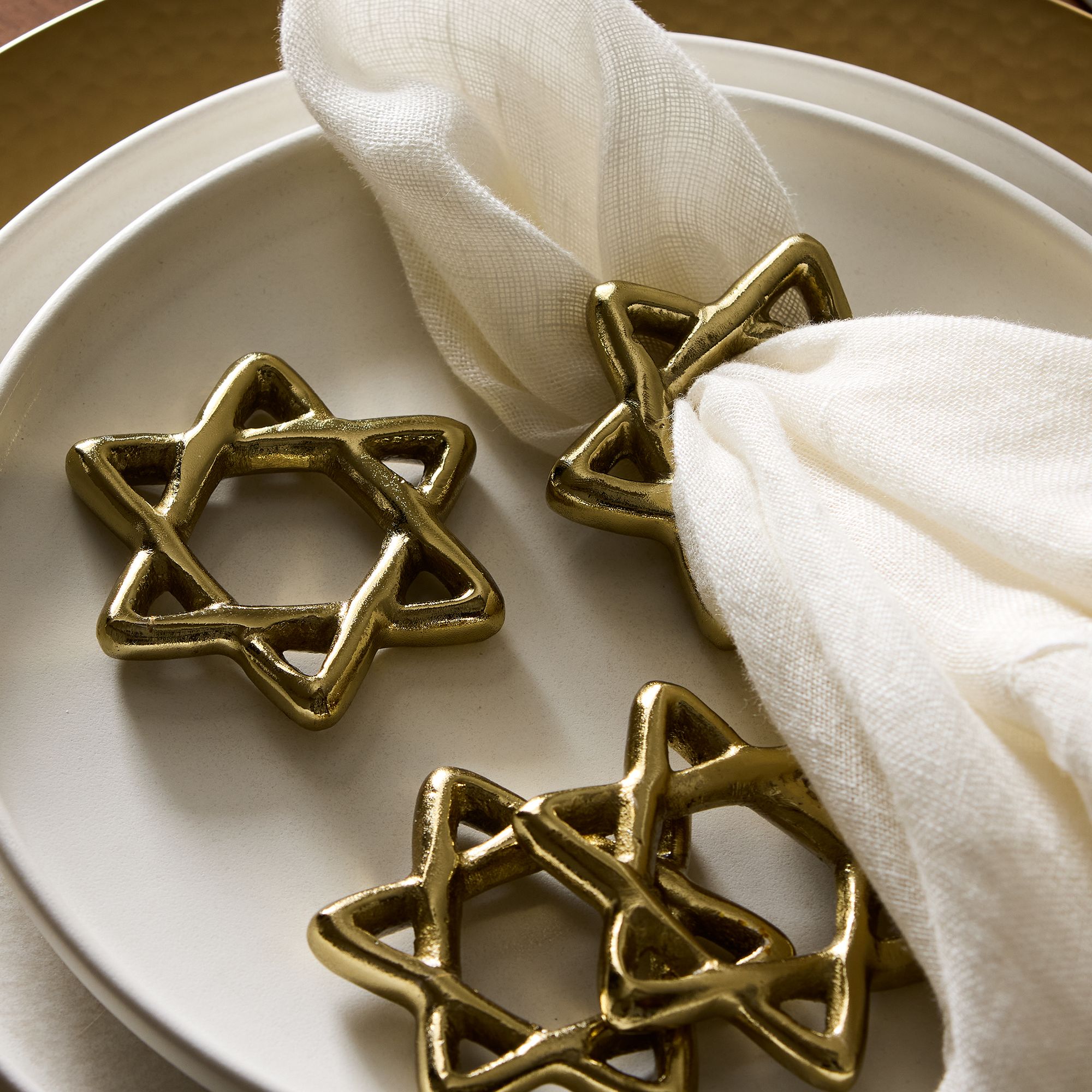 Four brass Star of David shaped napkin holders with a napkin on a plate