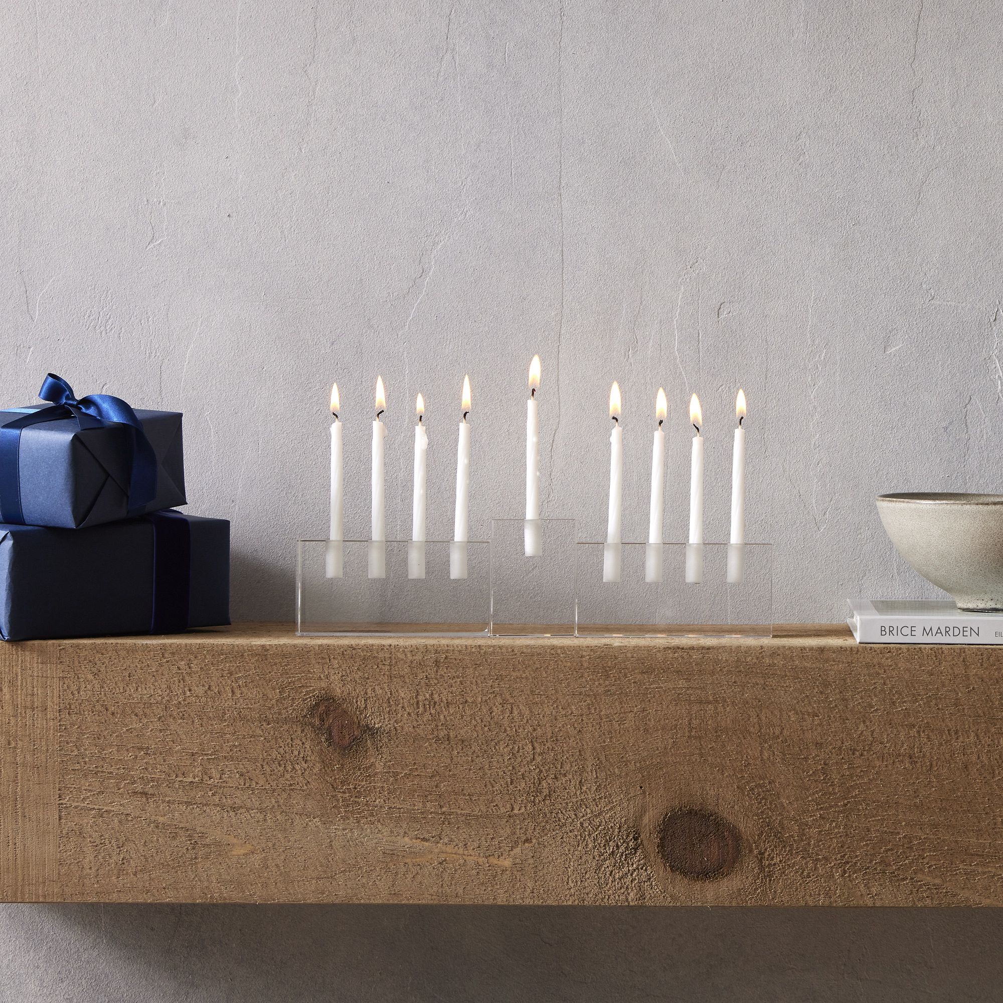 A clear glass menorah with nine lit candles in it