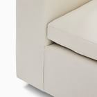 Corner view showing armrest and base of sofa with light beige fabric