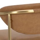Close-up of gold metal rail and tan leather upholstery stitch on a chair.